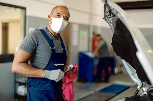 Schwarzer Automechaniker, der während der Arbeit in einer Werkstatt eine Schutzmaske trägt