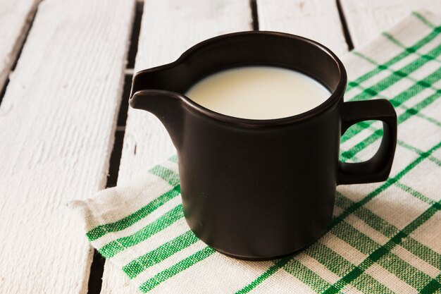 Schwarzer Becher Milch über der Serviette auf dem Holztisch