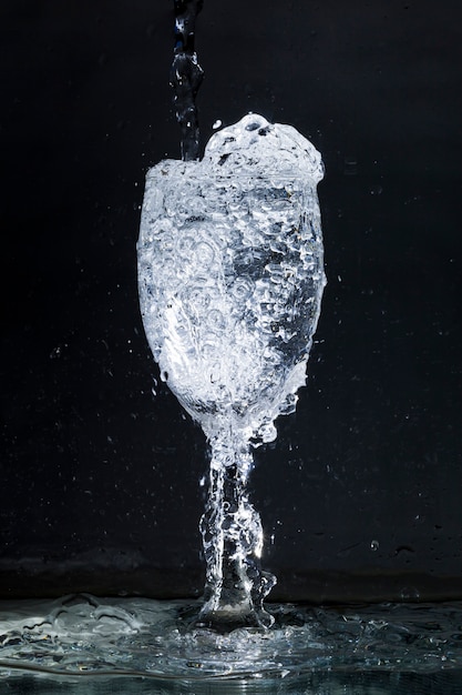 Schwarzer Hintergrund mit überfließendem Glas Wasser