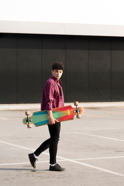 Schwarzer Jugendlicher im karierten Hemd gehend mit longboard