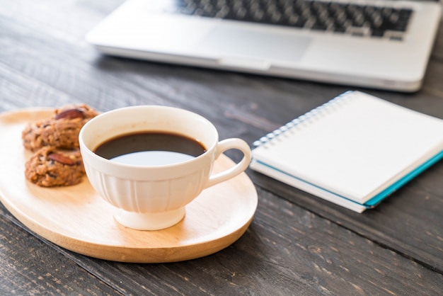 schwarzer Kaffee und Kekse mit Laptop und Notizbuch