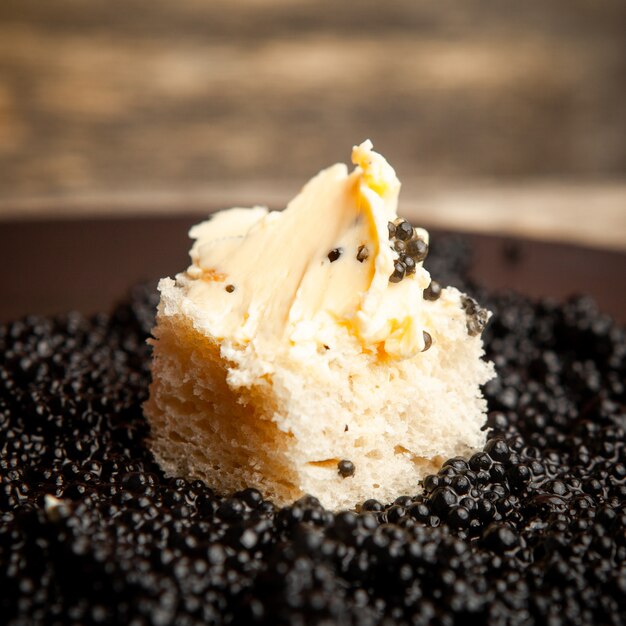 Schwarzer Kaviar der Seitenansicht mit Brot und Butter auf dunklem Hintergrund.