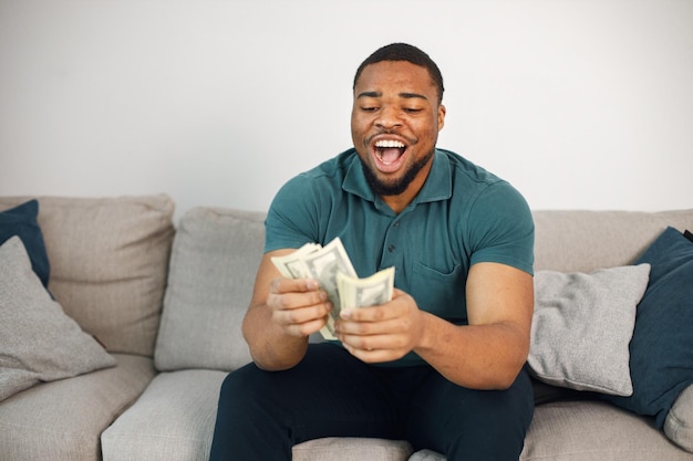 Schwarzer Kerl sitzt auf einer Couch im Wohnzimmer und hält ein Bargeld in der Hand