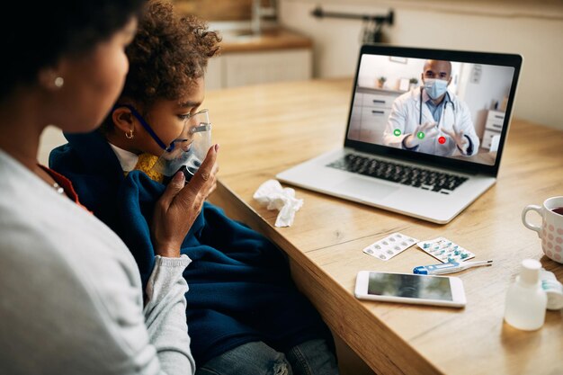 Schwarzer Kinderarzt spricht per Videoanruf mit der Mutter, die ihrer Tochter zu Hause eine Inhalationstherapie gibt