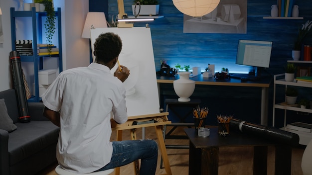 Schwarzer Künstler mit Bleistift auf Leinwand, um Vase zu zeichnen