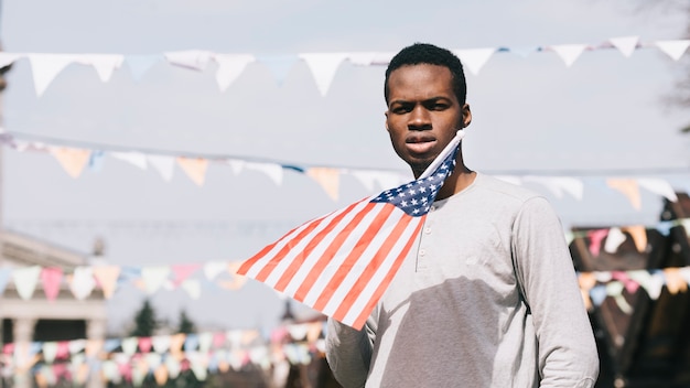 Kostenloses Foto schwarzer mann, der amerikanische flagge hält und kamera betrachtet