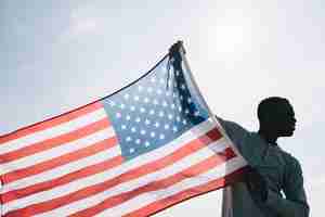 Kostenloses Foto schwarzer mann, der breite wellenartig bewegende amerikanische flagge hält