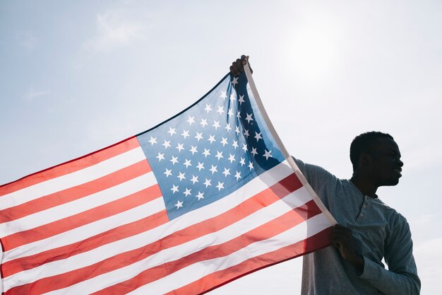 Schwarzer Mann, der breite wellenartig bewegende amerikanische Flagge hält