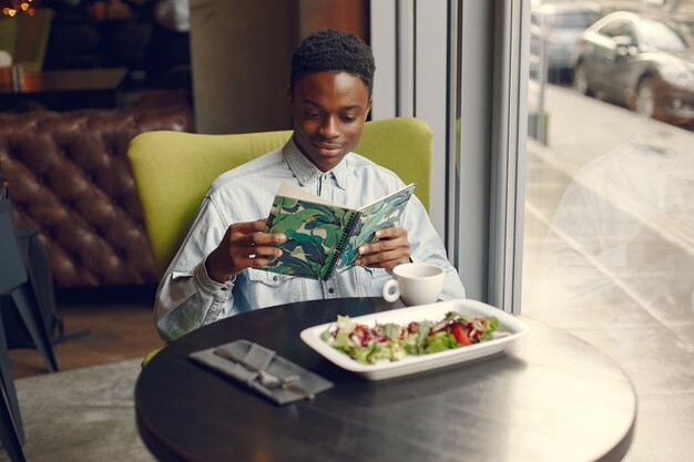 Schwarzer Mann, der in einem Café sitzt und einen Gemüsesalat isst