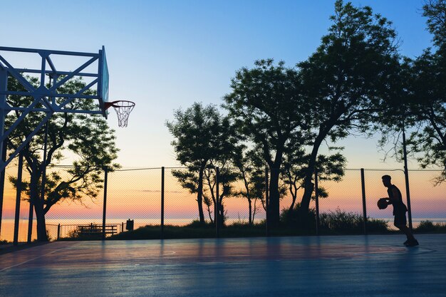 Schwarzer Mann, der Sport treibt, Basketball auf Sonnenaufgang, Silhouette spielend