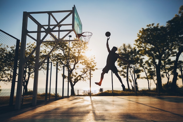 Schwarzer Mann, der Sport treibt, Basketball auf Sonnenaufgang spielt, Silhouette springt