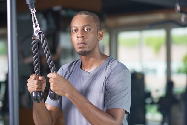 Schwarzer Mann, der Turnhallenausrüstung verwendet und Kamera betrachtet