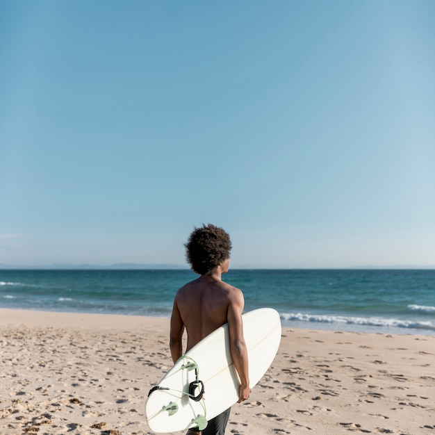 Schwarzer nachdenklicher Mann mit dem Surfbrett, das weg schaut