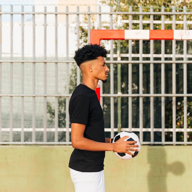 Schwarzer nachdenklicher Sportler, der Ball am Sportplatz hält