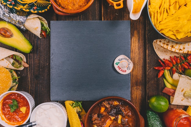 Schwarzer schiefer umgeben durch vielzahl des köstlichen mexikanischen lebensmittels auf brauner tabelle