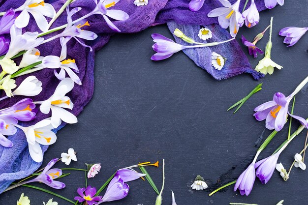 Schwarzer strukturierter Hintergrund mit lila gefärbtem Stoff und Frühlingsblumen