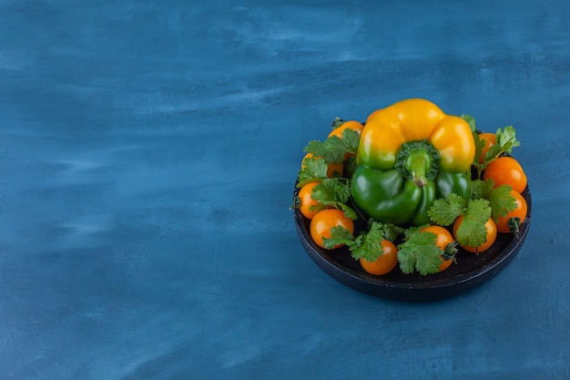 Schwarzer Teller mit Paprika und Kirschtomaten auf Blau.