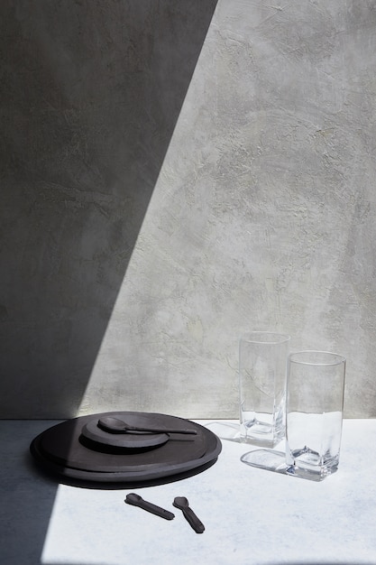 schwarzer Teller und zwei Glasbecher auf einem weißen Tisch, auf den der Schatten fällt