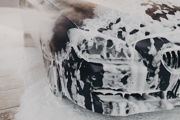 Schwarzes auto in weißem schneeschaum beim autowaschen und reinigen im freien