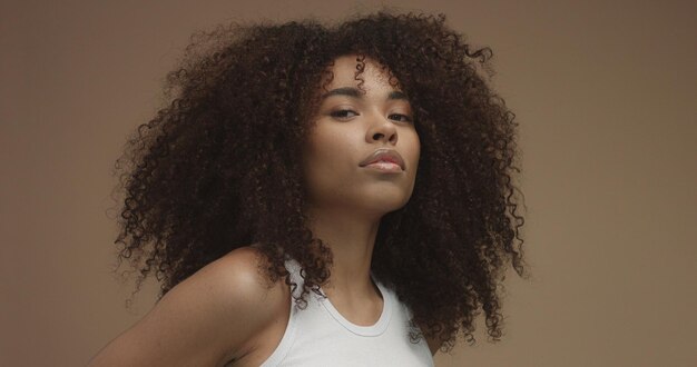 Schwarzes Frauenporträt der gemischten Rasse mit dem großen lockigen Haar des Afrohaares im beigen Hintergrund