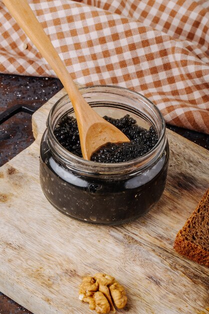 Schwarzes Kaviarglas der Seitenansicht mit Roggenbrot der Holzoberfläche und Walnuss auf einem Brett