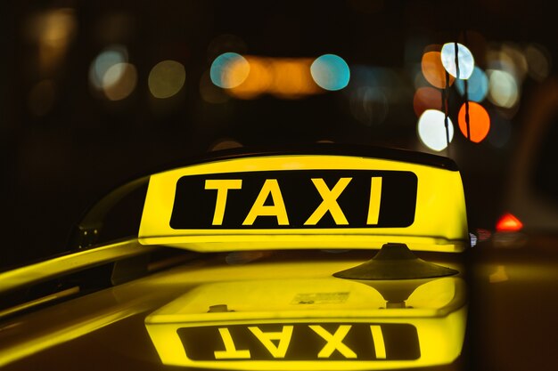 Schwarzes und gelbes Zeichen des Taxis in der Nacht auf einem Auto platziert