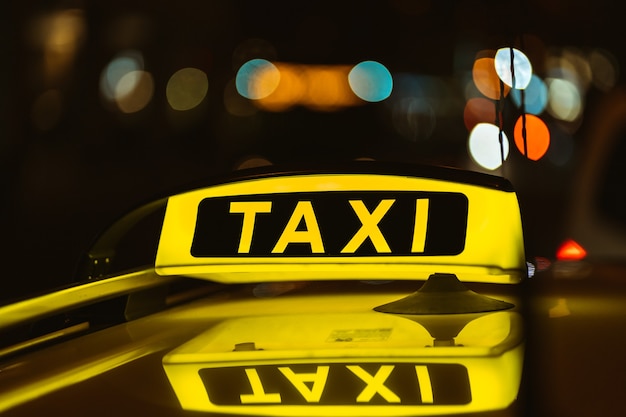 Schwarzes und gelbes Zeichen des Taxis in der Nacht auf einem Auto platziert