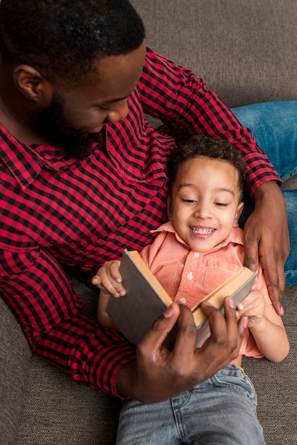 Kostenloses Foto schwarzes vater- und nettes sohnlesebuch auf couch