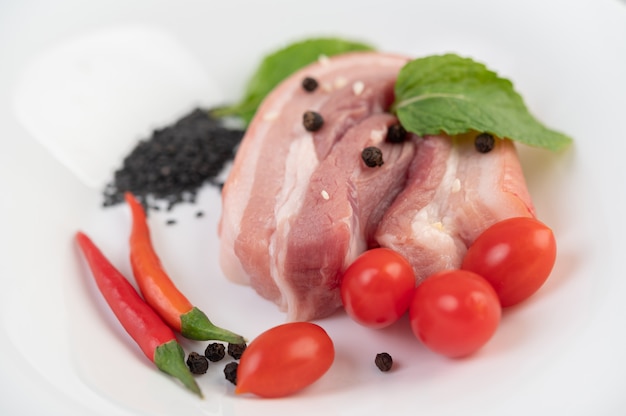 Schweinebauch in einer weißen Schale mit Pfeffersamen Tomaten und Gewürzen.