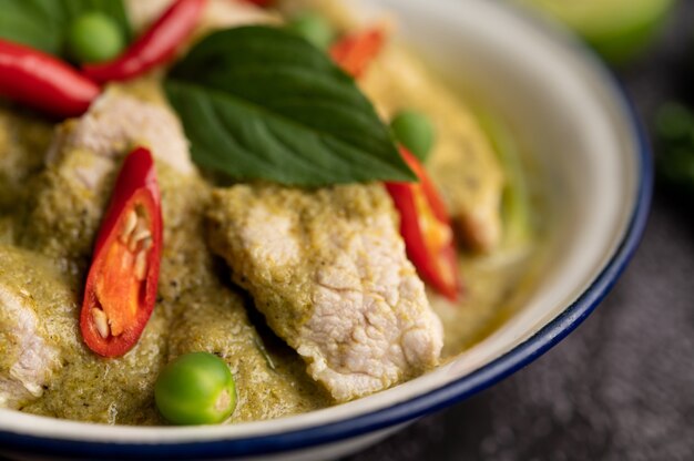 Schweinegrüncurry in einer weißen Schüssel mit Gewürzen auf einem schwarzen Zementhintergrund