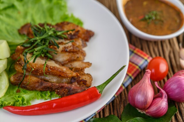 Schweinehals auf einem weißen Teller mit roten Zwiebeln, Tomaten und Chili auf dem Holztisch gegrillt.