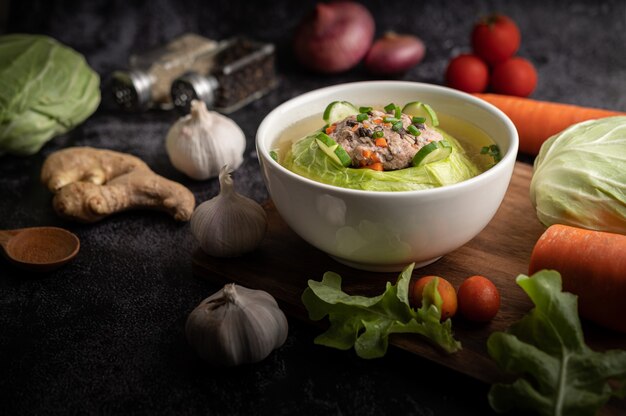 Schweinekohlsuppe mit Karotten, gehackten Frühlingszwiebeln, Gurke in einem Holzteller auf einem Holzteller