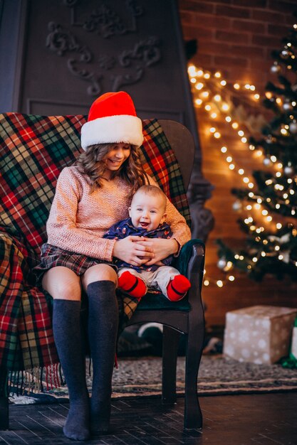 Schwester mit dem kleinen Bruder, der auf einem Stuhl durch Weihnachtsbaum sitzt