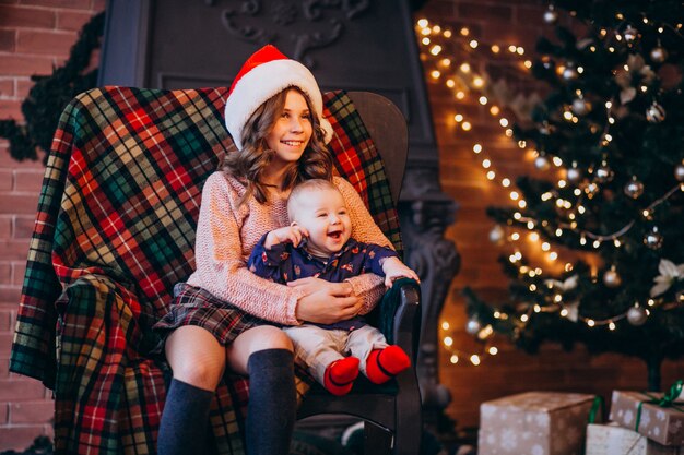 Schwester mit dem kleinen Bruder, der auf einem Stuhl durch Weihnachtsbaum sitzt