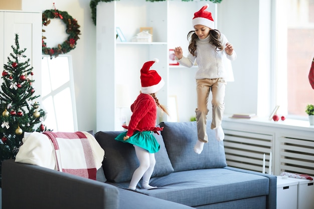 Schwestern springen und spielen auf der Couch, Mädchen mit Weihnachtsmütze