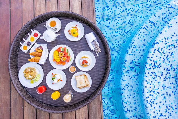 Schwimmendes Frühstückstablett um Außenpool mit Brotfrucht-Ei-Kaffee und Saft