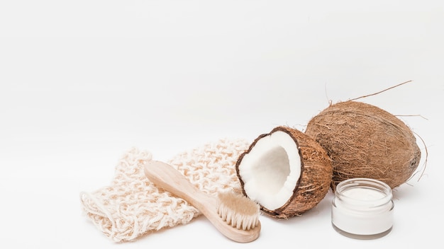 Scrub-Handschuh; Bürste; Kokosnuss und Feuchtigkeitscreme auf weißem Hintergrund