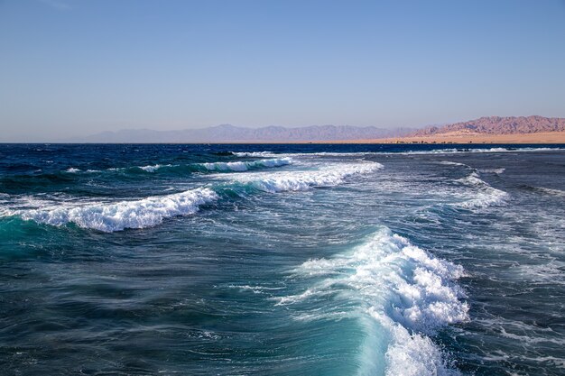 Seelandschaft mit strukturierten Wellen und Bergsilhouetten am Horizont.