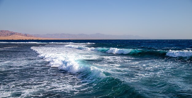 Seelandschaft mit strukturierten Wellen und Bergsilhouetten am Horizont.