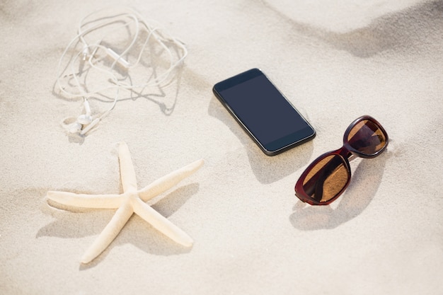 Kostenloses Foto seestern, sonnenbrille, kopfhörer und handy gehalten auf sand