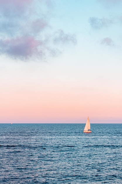 Segelboot segeln auf dem welligen Ozean unter dem wunderschönen rosa bewölkten Himmel