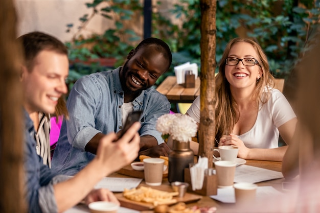 Sehen Sie sich mit Kollegen ein lustiges Video im Internet im Café auf der Terrasse mit leckerem Essen an