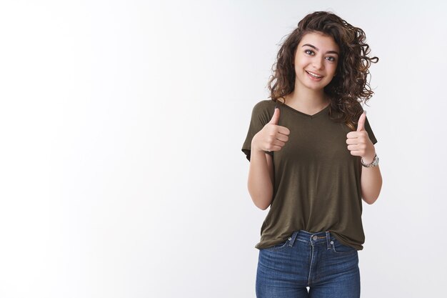 Sehr gut. Fröhliche, unterstützende süße armenische Freundin mit lockigen Haaren zeigt Daumen hoch, ermutigt den Freund, der gut lächelt