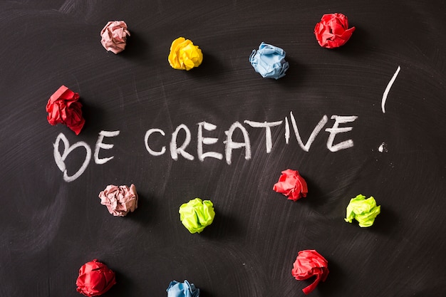 Seien Sie Kreativitätswort mit buntem zerknittertem Papierball auf Tafel