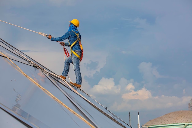 Seilzugangshöhensicherheit für männliche arbeiter, die mit einem knotensicherheitsgurt, dachabsturzsicherung und absturzsicherungs-ankerpunktsystemen verbunden sind, die zum aufsteigen bereit sind, öltankkuppel auf der baustelle