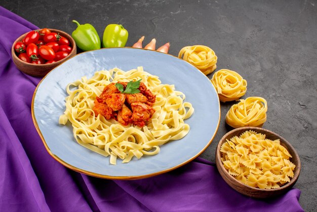 Seite Nahaufnahme Teller mit Essen Schüssel Tomaten Zwiebel Kugelpfeffer neben den Nudeln und Teller Nudeln mit Fleisch auf der lila Tischdecke