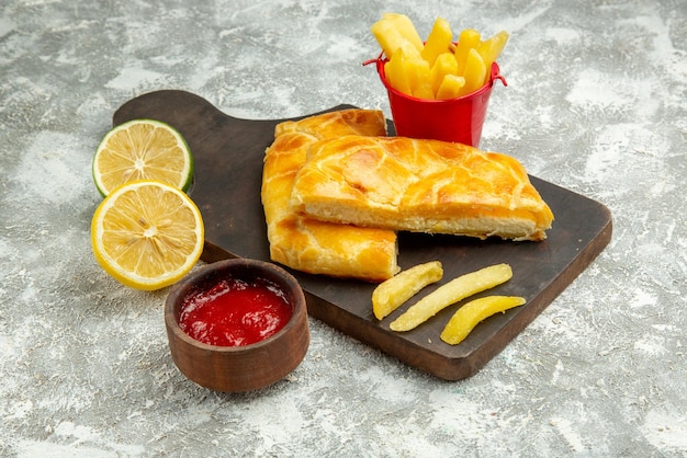 Kostenloses Foto seite nahaufnahme torten pommes frites schüssel ketchup zitrone und pommes frites und appetitliche torten auf dem küchenbrett auf dem grauen tisch