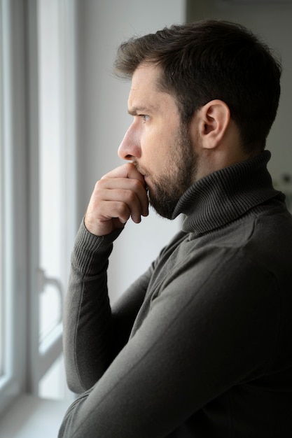 Seitenansicht ängstlicher Mann, der aus dem Fenster schaut