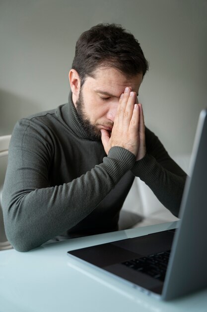 Seitenansicht ängstlicher Mann, der zu Hause mit Laptop arbeitet