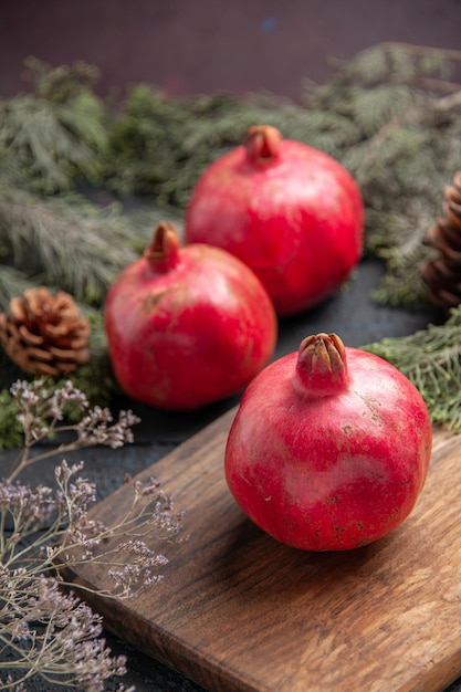 Seitenansicht aus der Ferne Granatapfel und Borded Granatapfel auf Küchenbrett neben zwei Granatäpfeln und Fichtenzweigen mit Zapfen auf grauem Tisch